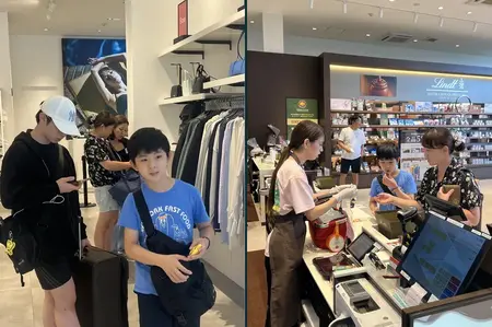 哥哥一手滑手機、一手拉著行李箱。弟弟背著自己的包走在前面，媽媽買了巧克力給他試吃。