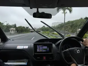 右駕方向盤自己握著，擋風玻璃外是空的公路和棕櫚樹。OTS 租的車。